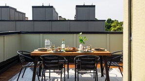 Un espace de restauration aménagé sur le toit, avec une table en bois prévue pour quatre personnes, entourée de chaises noires.
