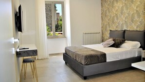 A modern bedroom with a large bed, a bedside table, a chair, and a window with a view of greenery. - Nice apartment for 6 guests with A/C, TV, balcony and pets allowed (Formia)