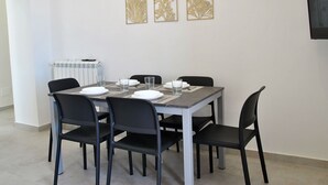A dining area with a rectangular table set for four, surrounded by black chairs. There are three decorative wall panels above the table. - Nice apartment for 6 guests with A/C, TV, balcony and pets allowed (Formia)