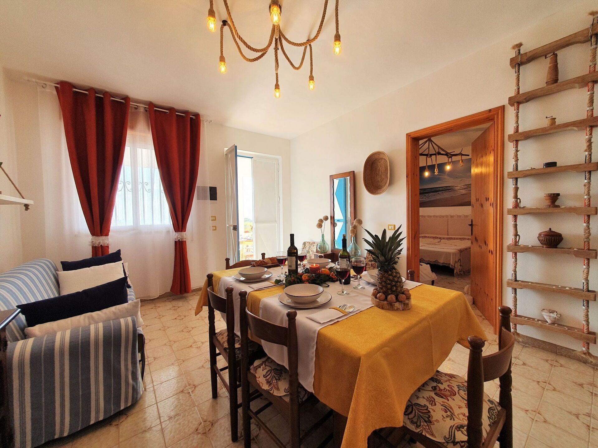 A dining area with a table set for four, a chandelier, and a rustic wooden shelf with pottery.
