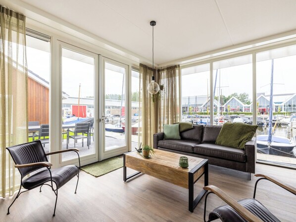 A modern living room with a sofa, chairs, a coffee table, and large windows with a marina view.