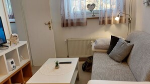 A living room with a sofa, a radiator, a ceiling fan, and a shelf with various items.