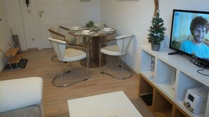 A modern living room with a dining table, two white chairs, a television, and a small Christmas tree.