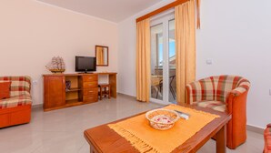 Una sala de estar con un sofá, una mesa de madera con una cesta, un televisor y un ventanal corredero a un balcón.