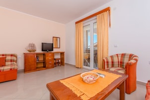 A living room with a sofa, a wooden table with a basket, a television, and a sliding glass door to a balcony.