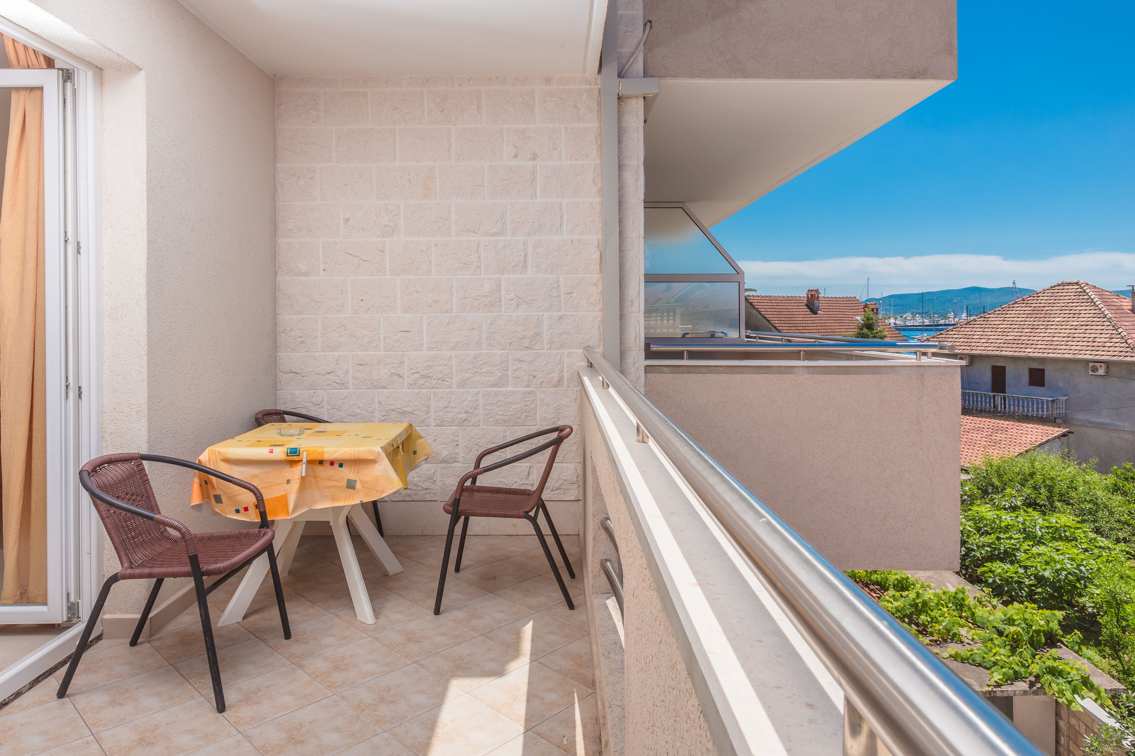 A balcony with a table and two chairs, a view of the city, and a clear sky.