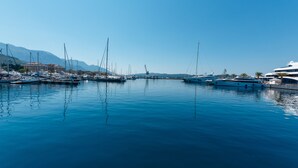 Un puerto deportivo con varias embarcaciones amarradas, cielo despejado y montañas al fondo.