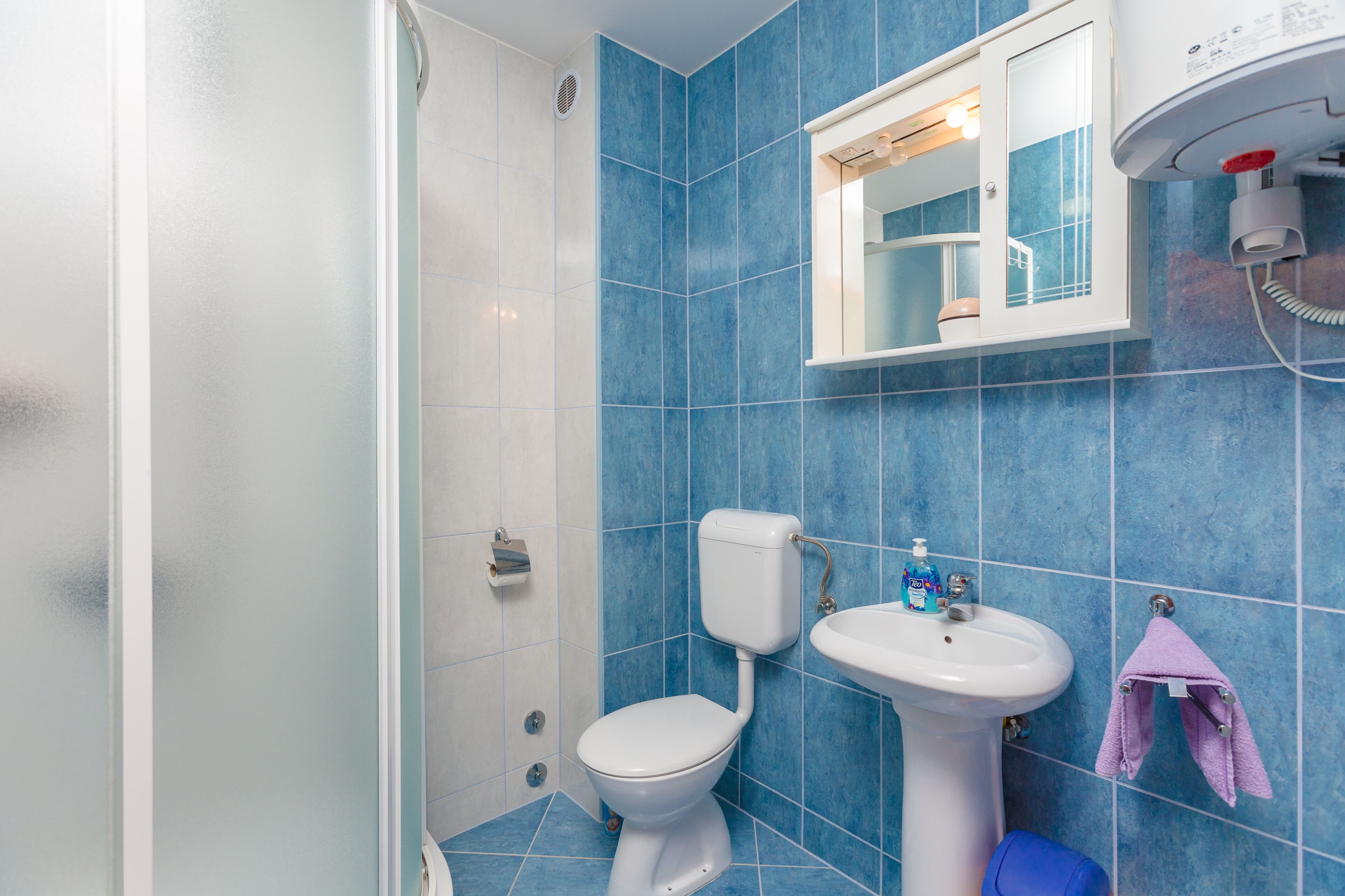 Un baño con azulejos azules, un inodoro blanco, un lavamanos blanco y un perchero para toallas.