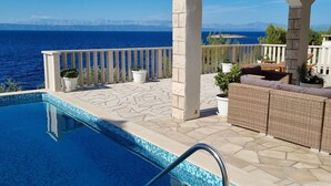Une piscine avec vue sur la mer et les montagnes, un espace extérieur aménagé et des plantes en pot.