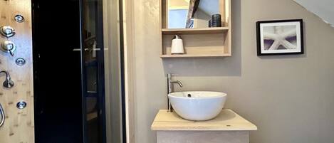 Une salle de bain avec un meuble-lavabo en bois, un lavabo blanc, un miroir et un tableau encadré au mur.