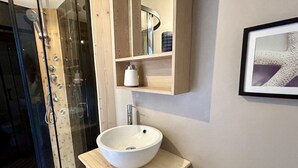 Une salle de bain avec une douche à parois de verre, un lavabo blanc posé sur un meuble en bois, un miroir au-dessus du lavabo et un tableau encadré au mur.