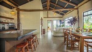 A spacious kitchen with a central island, wooden stools, and a dining area with a wooden table set for six. - Cabañas Caeli, Peaceful Rainforest Retreat with Stunning Views (Peñas Blancas)