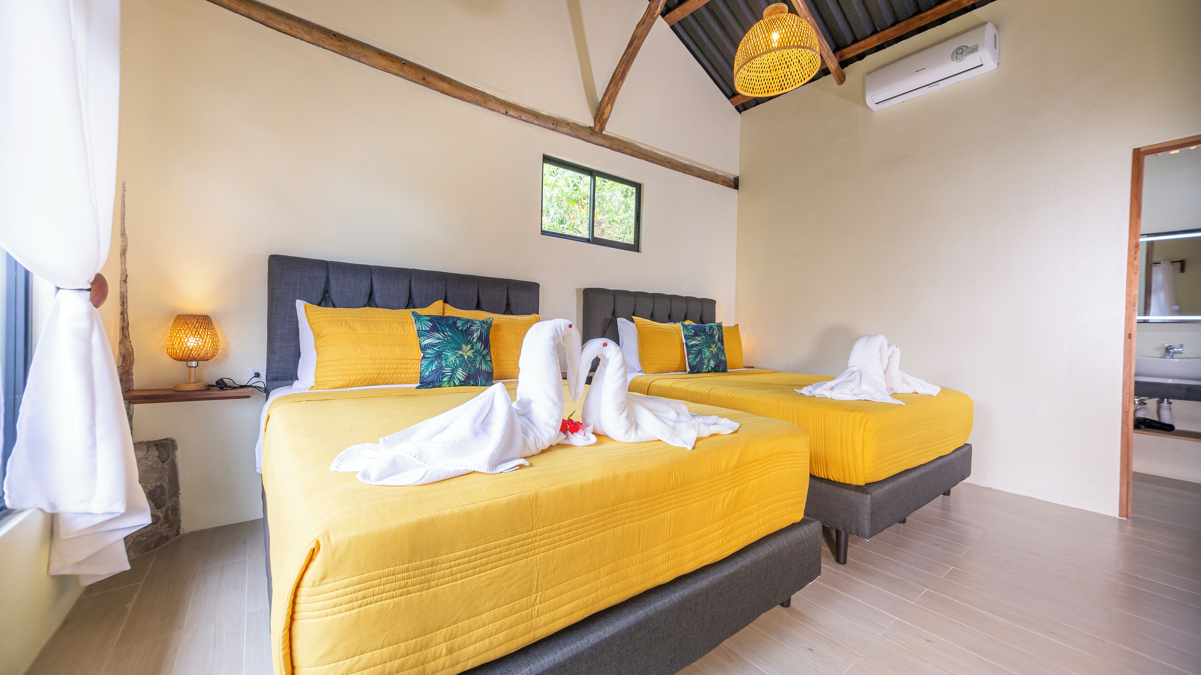 Two beds with yellow bedding, a small window, and an air conditioning unit.