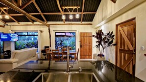 A modern kitchen with a central island, stainless steel sink, wooden ceiling beams, and a large window overlooking greenery. - Cabañas Caeli, Peaceful Rainforest Retreat with Stunning Views (Peñas Blancas)