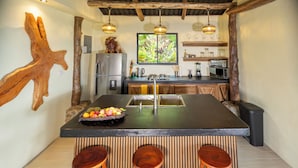 A kitchen with a central island, wooden stools, a refrigerator, a sink, and hanging pendant lights. - Cabañas Caeli, Peaceful Rainforest Retreat with Stunning Views (Peñas Blancas)
