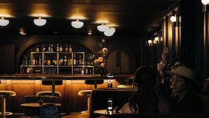A dimly lit bar area with wooden furniture, a bar counter with bottles, and a decorative vase with flowers. - Hotel Granada, a Member of Design Hotels (Atlanta)