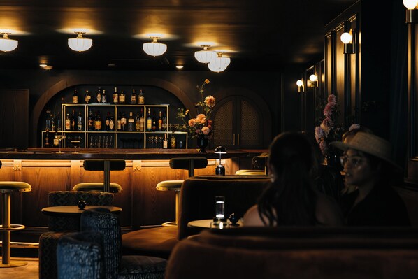 A dimly lit bar area with wooden furniture, a bar counter with bottles, and a decorative vase with flowers. - Hotel Granada, a Member of Design Hotels (Atlanta)