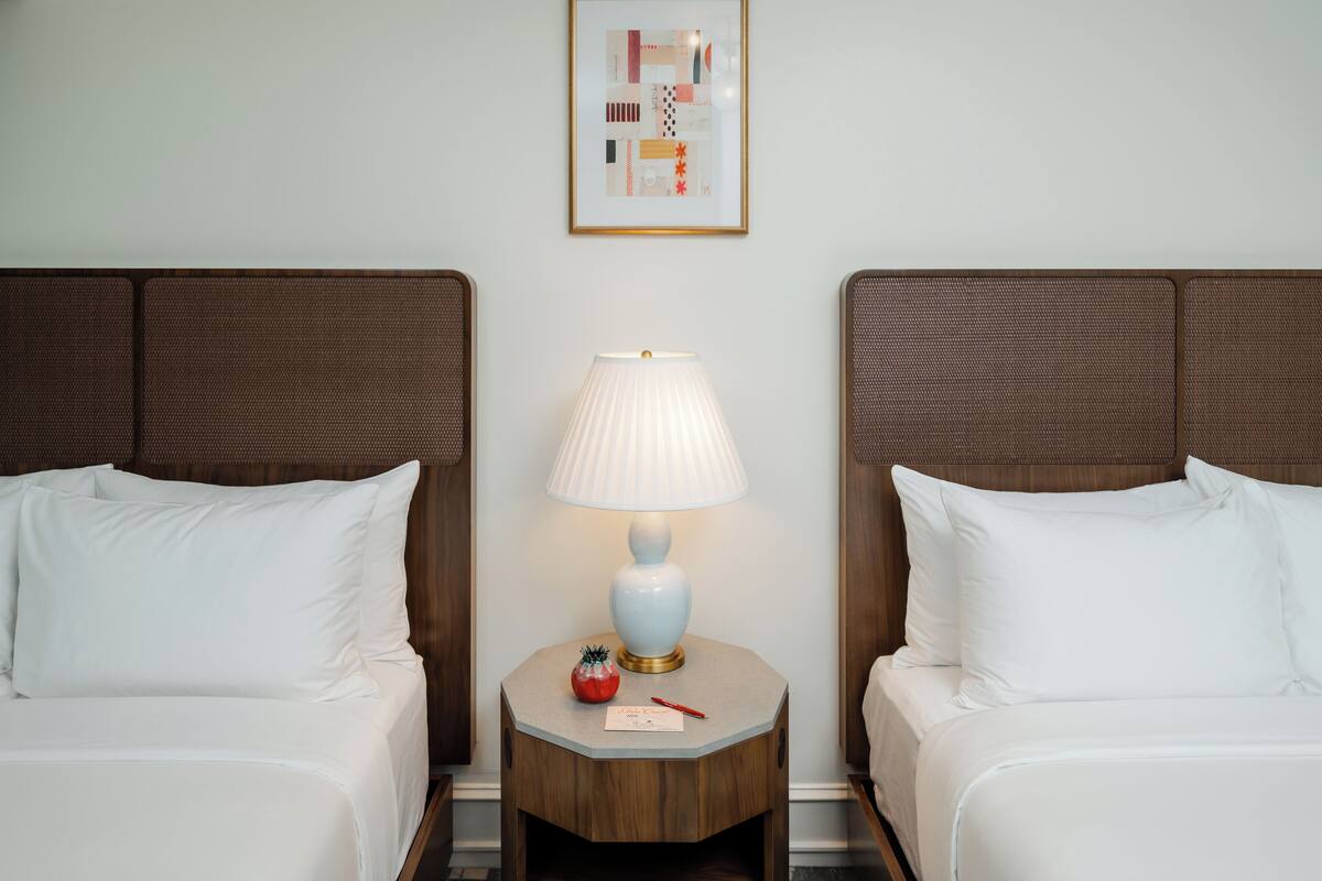 A hotel room with two beds, a nightstand with a lamp, and a framed picture on the wall.