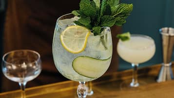 A bar setting with a drink garnished with lemon and mint, a menu, and a bartender preparing another drink.