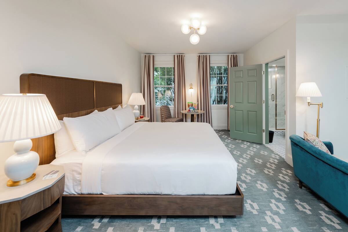 A hotel room with a large bed, two bedside lamps, a nightstand, a chair, a small table, and a blue sofa.