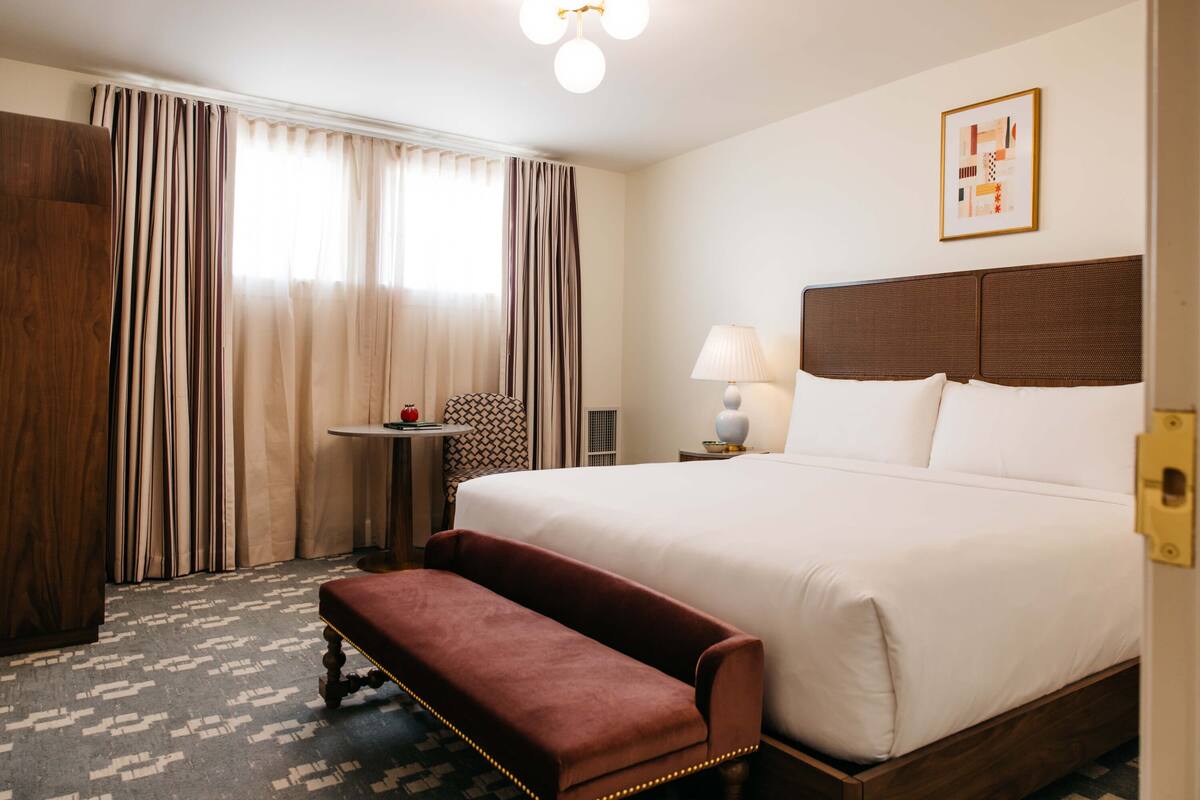 A hotel room with a large bed, a bench, a small table, a lamp, and a framed picture on the wall.