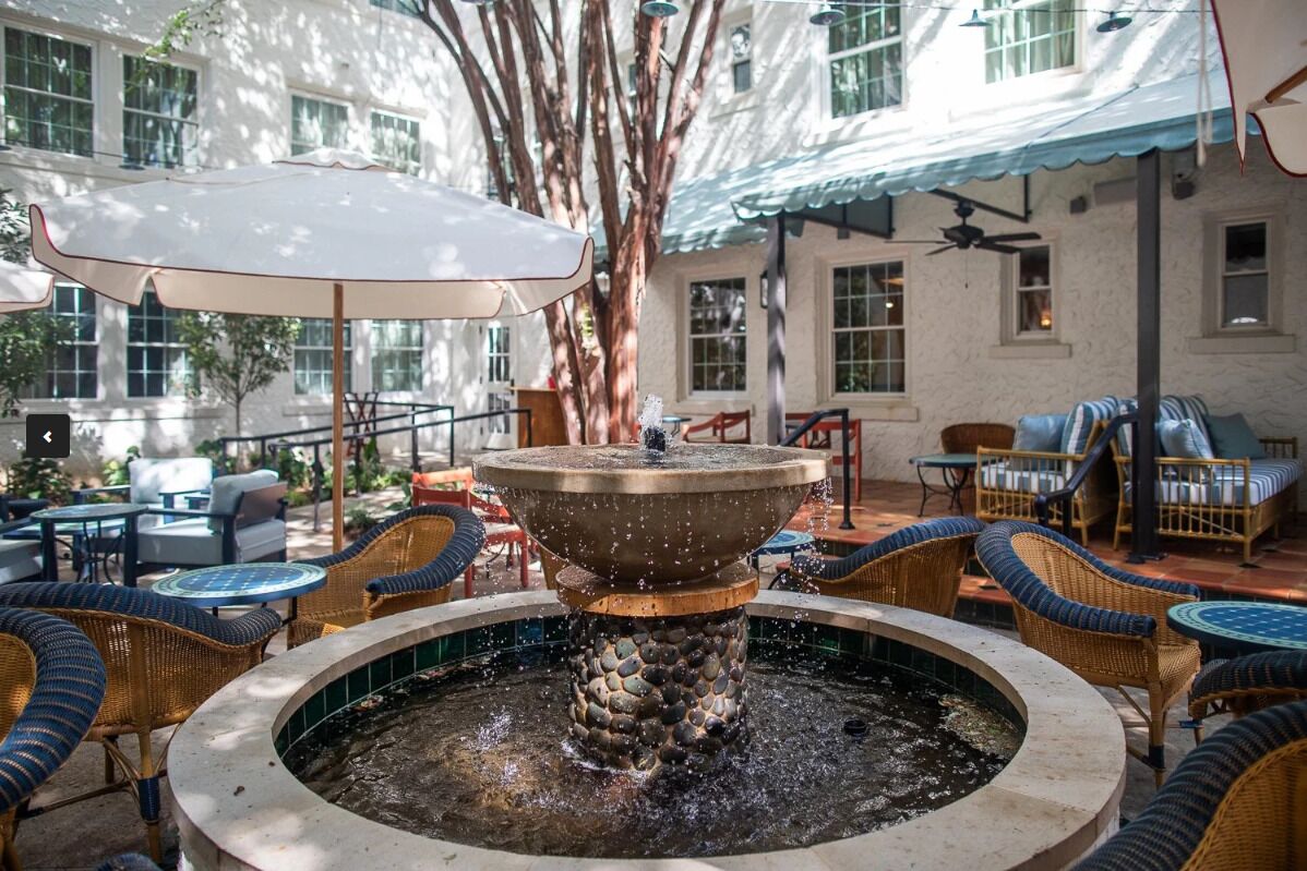 A courtyard with a central fountain, wicker furniture, and a building with large windows in the background.