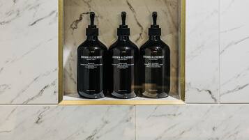 Bagno con rivestimento in marmo e ripiano contenente tre prodotti 'Grown Alchemist'.