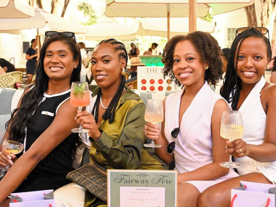 Un groupe de personnes est assis à une table à l’extérieur, devant des boissons, entouré de parasols et d’un présentoir à menus.