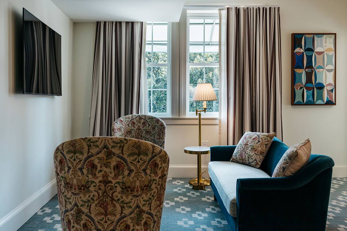 A room with patterned chairs, a sofa, a lamp, and a painting on the wall.