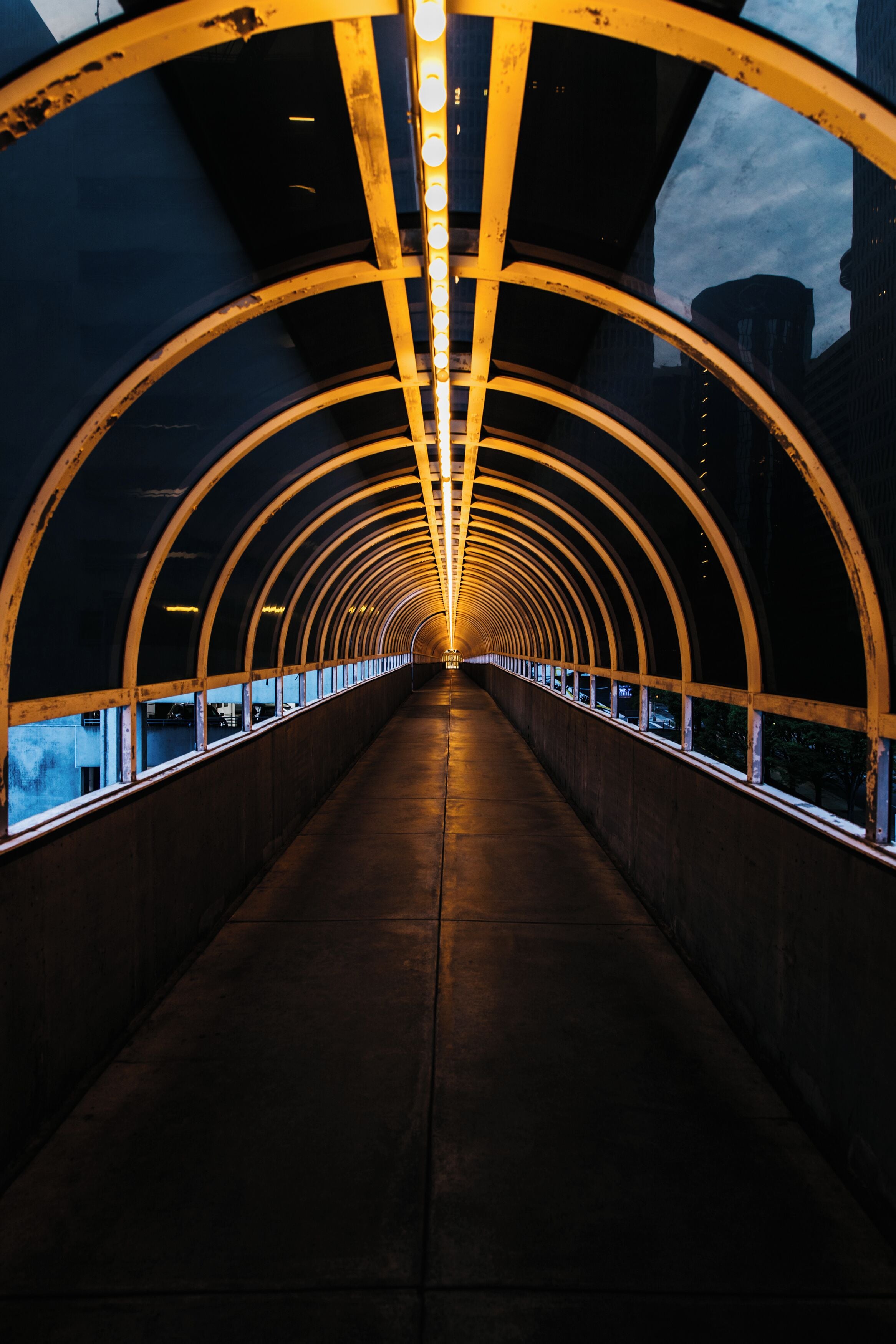 A covered pedestrian bridge with a series of arches and lights along the underside.