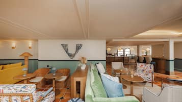 A spacious living area with a sofa, chairs, and a dining table. There is a kitchen area in the background.