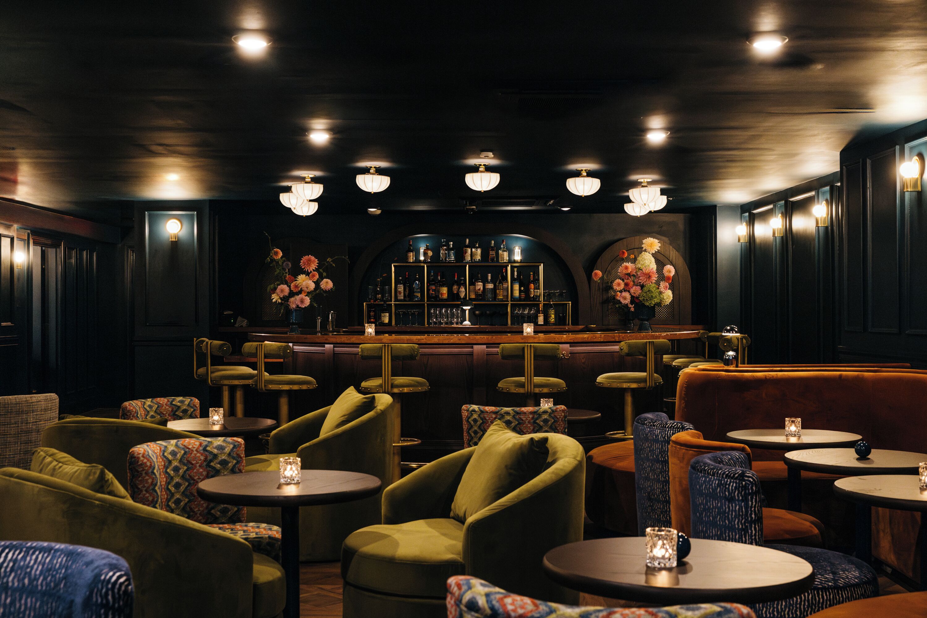 A bar area with round tables, cushioned chairs, and a bar counter with bottles.