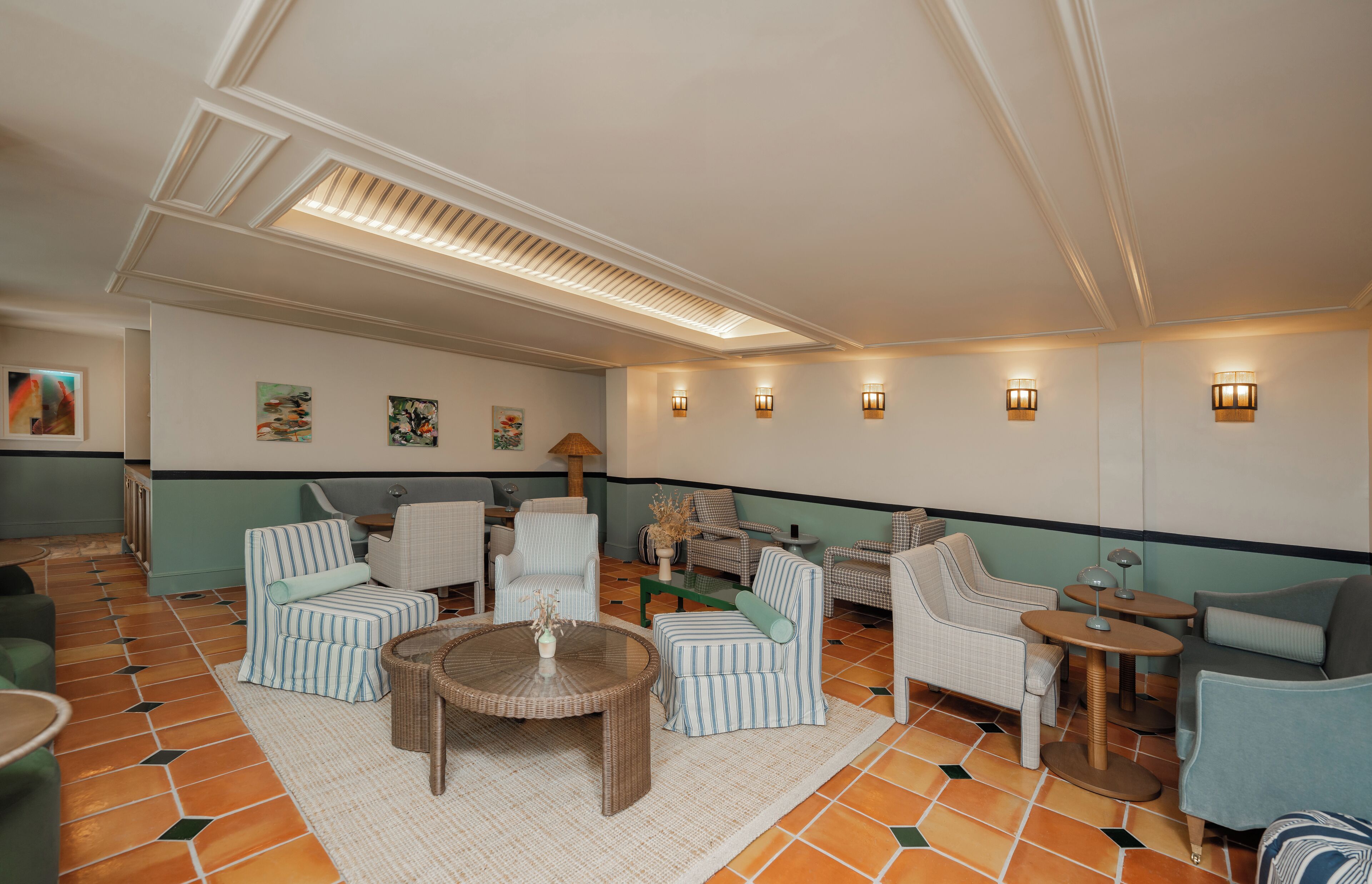 A well-lit lounge area with striped armchairs, a round table, and wall-mounted lights.
