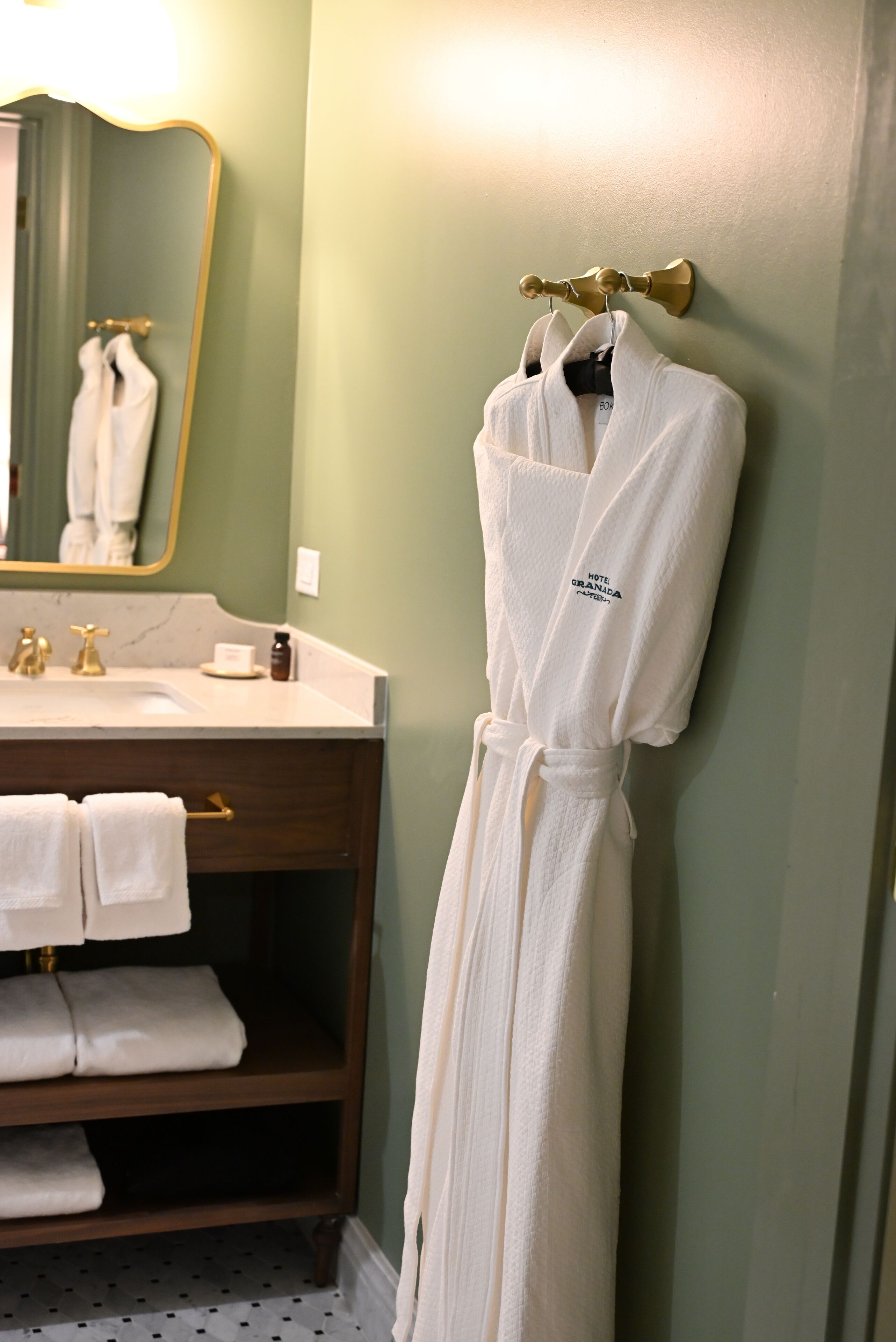 A bathroom with a sink, mirror, and a robe hanging on a hook.