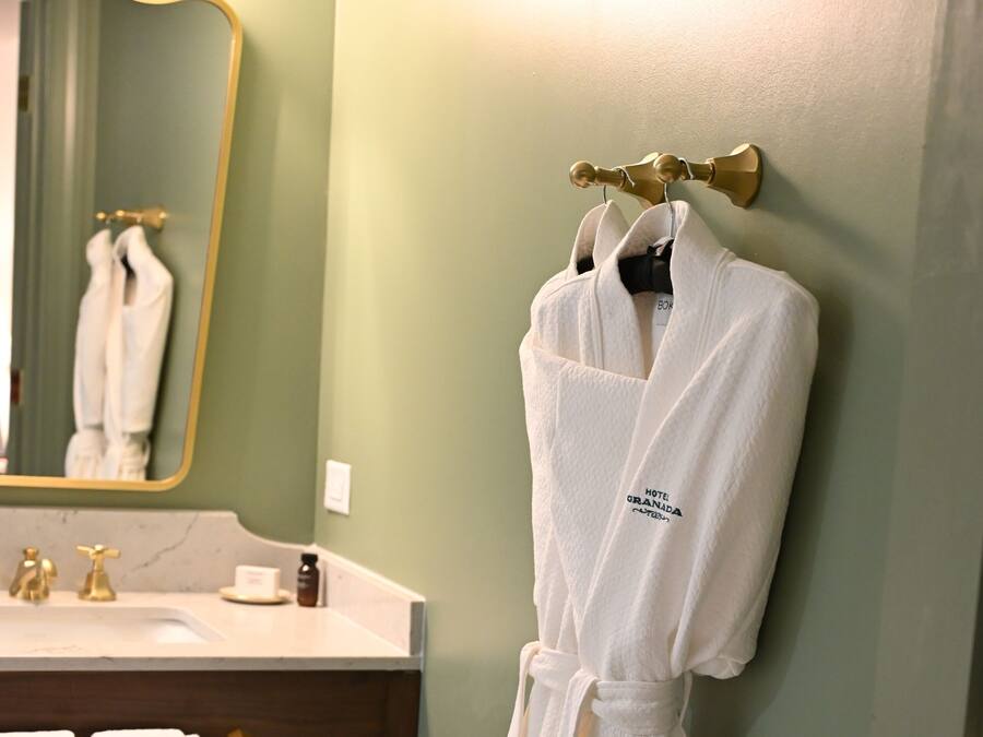 A bathroom with a sink, mirror, and a robe hanging on a hook.