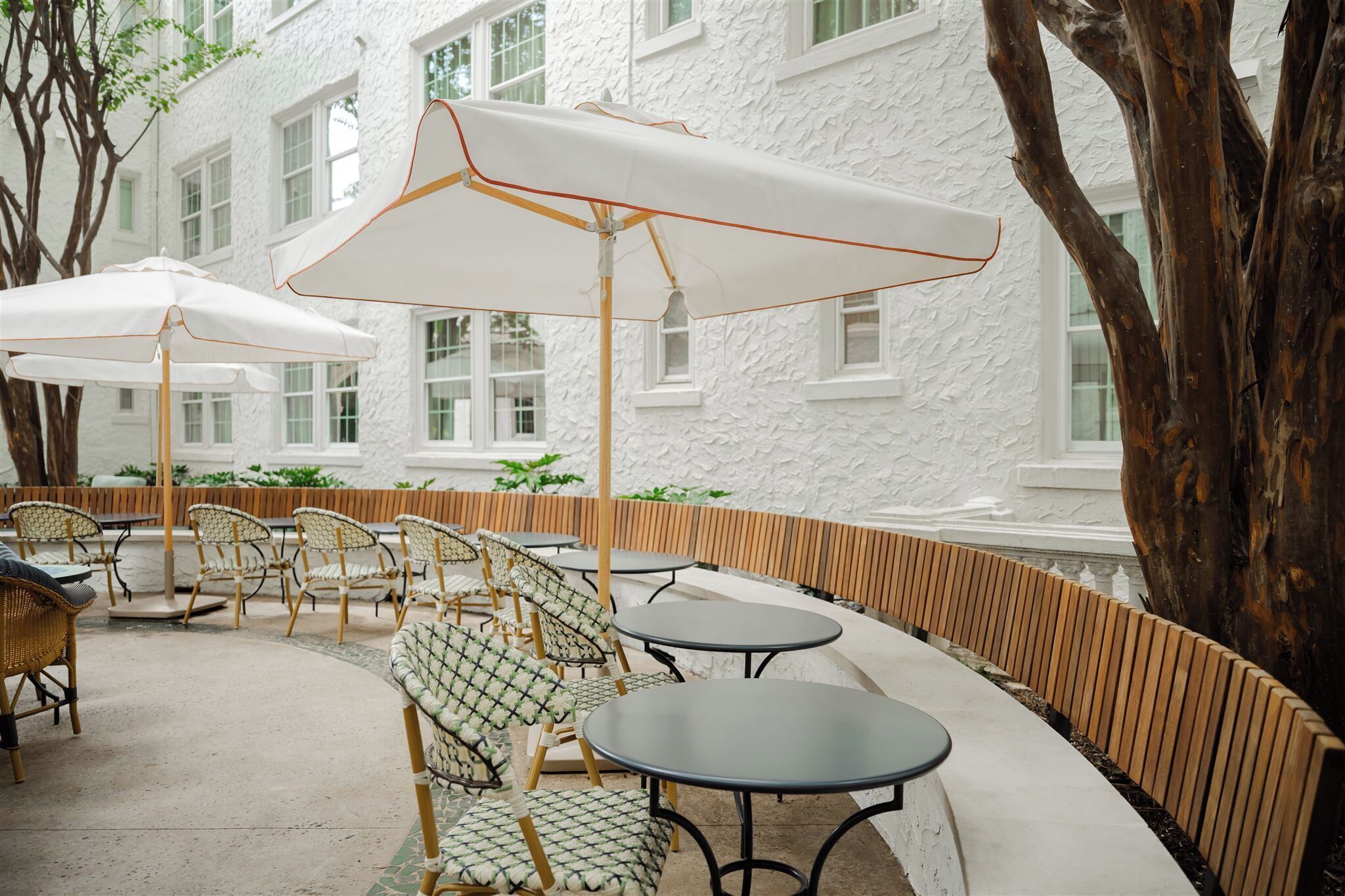 Outdoor seating with white umbrellas, wicker chairs, and a white building in the background.