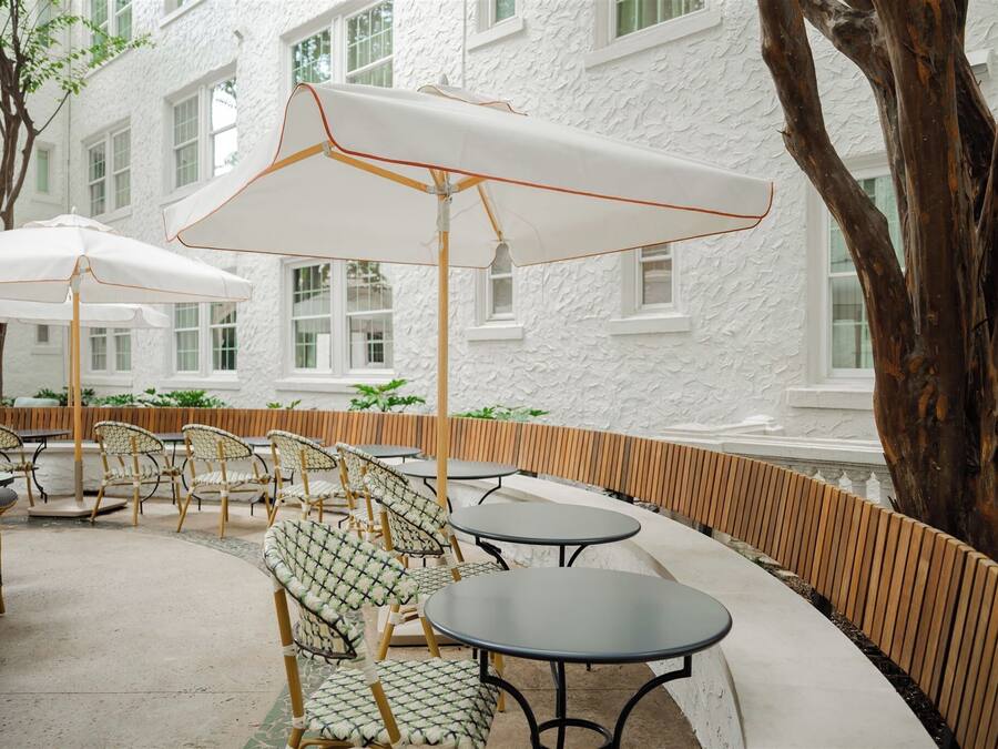 Outdoor seating with white umbrellas, wicker chairs, and a white building in the background.