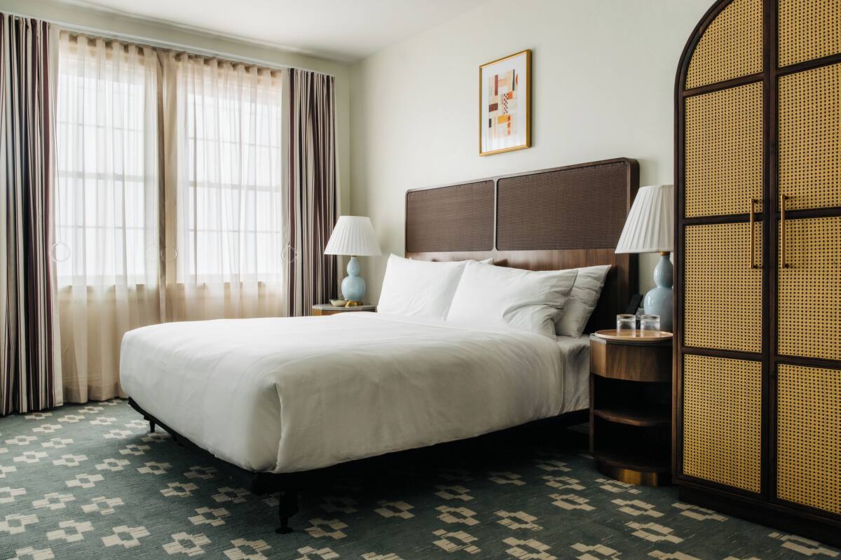 A hotel room with a large bed, two bedside lamps, a rattan partition, and a patterned carpet.