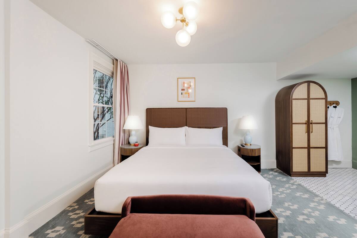 A hotel room with a large bed, bedside lamps, a wardrobe, and a framed picture on the wall.