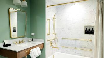 A bathroom with a vanity, two sinks, a bathtub, and a shower with gold fixtures.