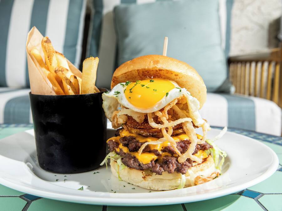 Une assiette avec un hamburger et des frites, une tasse noire et, à l’arrière-plan, un canapé à rayures bleues et blanches.