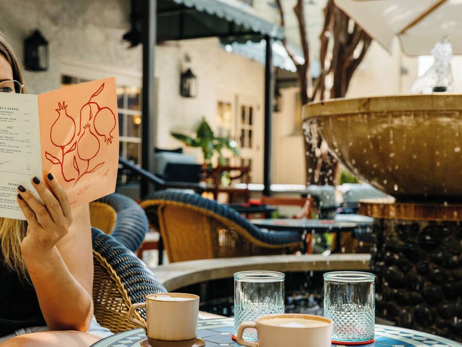 Una persona leyendo un menú en un café al aire libre con una fuente y mobiliario de mimbre.