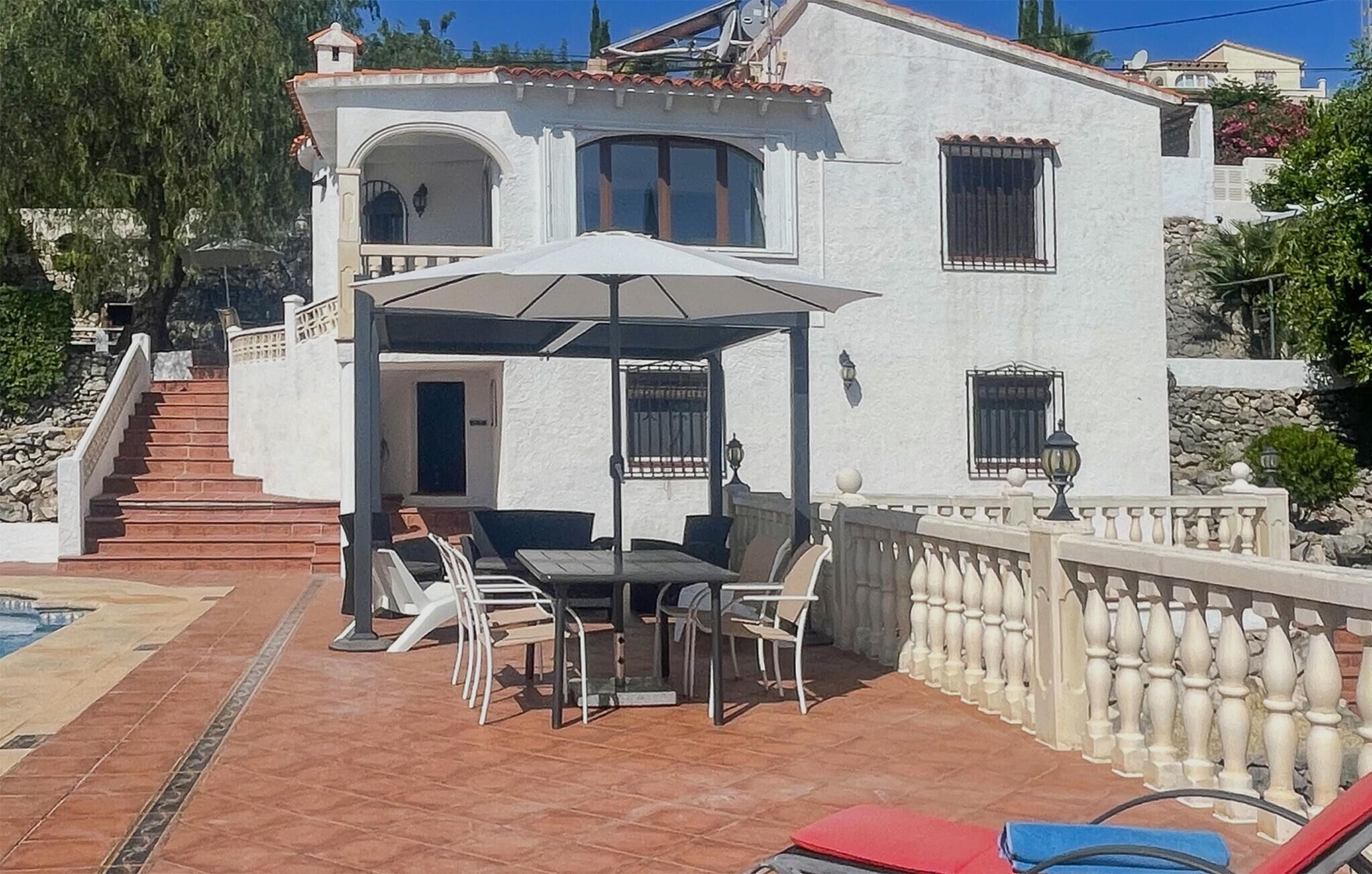 Ein zweistöckiges Gebäude mit einer Terrasse, die einen Tisch, Stühle, eine überdachte Sitzgelegenheit und einen Pool bietet.