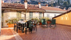 A terrace with a table and chairs, overlooking a hillside town with traditional buildings and mountains in the background. - Beautiful apartment for 6 guests with WIFI, TV and terrace (Bellano)