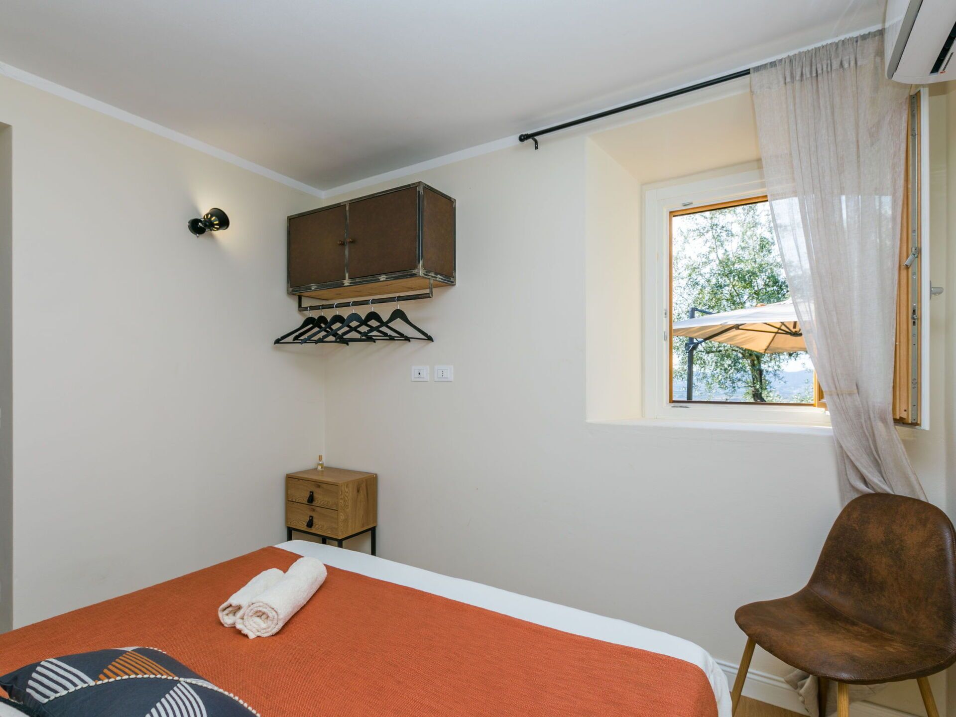A bedroom with a bed, a wooden cabinet, a chair, and a window with a view of trees.