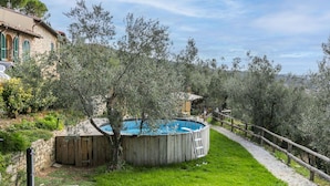 Un jardin avec une piscine en bois, entouré d’oliviers et délimité par un mur de pierres.