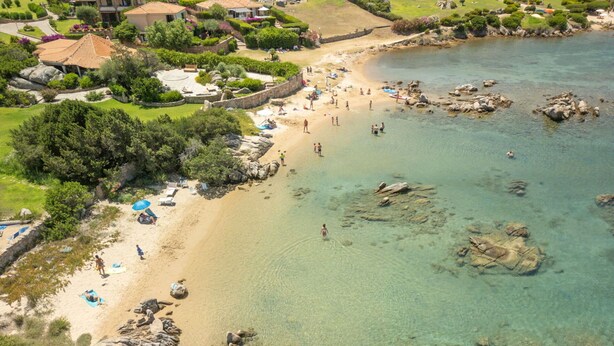 An aerial view of a beach with clear water, rocky areas, and a few people. - Nice apartment for 4 guests with pool, A/C, TV, patio and pets allowed (Olbia)