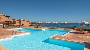 A pool area with clear blue water, sun loungers, and umbrellas. - Lovely apartment for 5 people with A/C, pool, TV, terrace and pets allowed (Olbia)