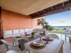 Een terras met een witte tafel gedekt voor vier personen, een witte bank en uitzicht op zee.