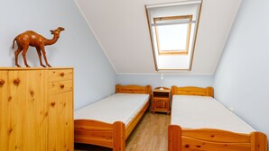 A small, triangular room with two wooden beds, a wooden dresser, and a skylight.